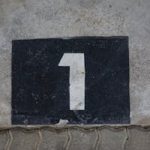 A weathered concrete wall with a bold number one painted on a black rectangular background.